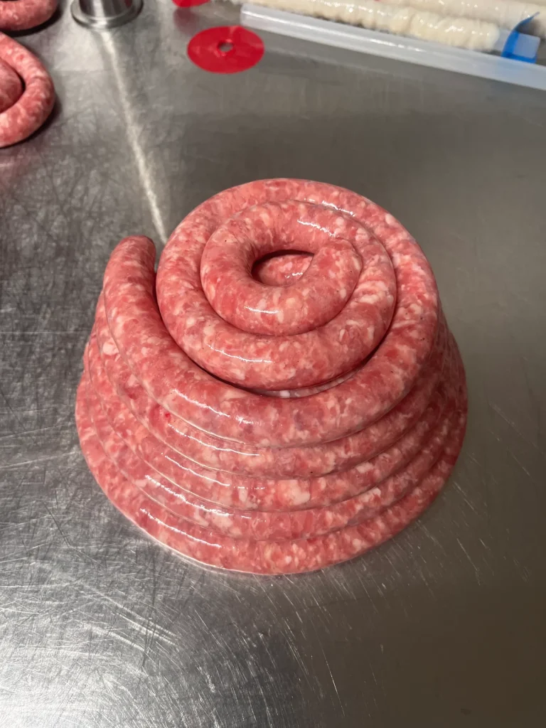 Une saucisse enroulée sur une surface en acier inoxydable, semblant fraîchement préparée et prête à être cuite.